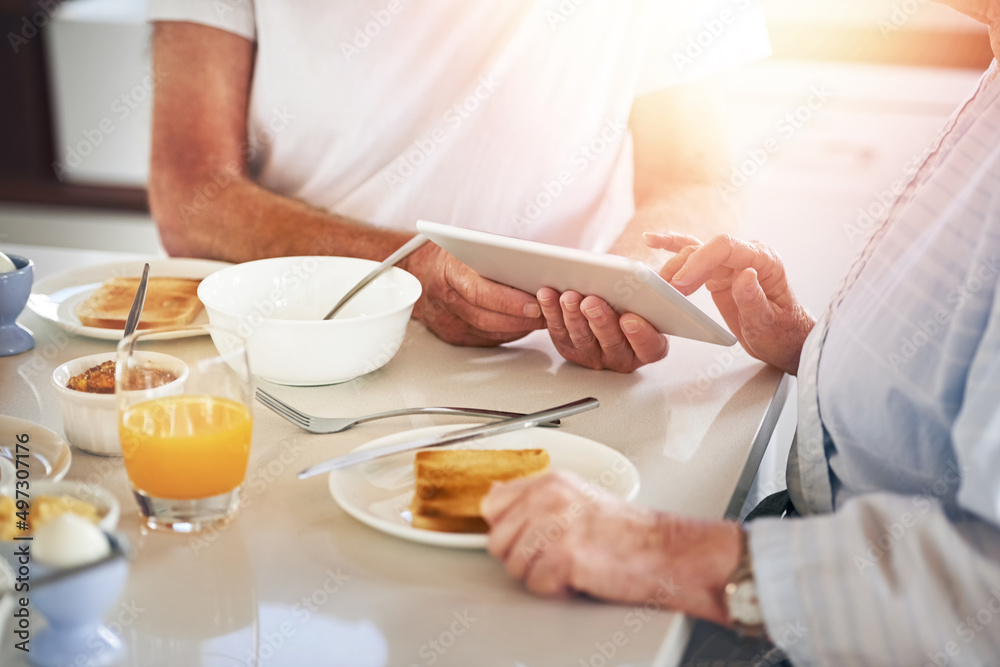 Browsing at breakfast. Closeup shot of a senior couple using a digital tablet while having breakfast at home.
