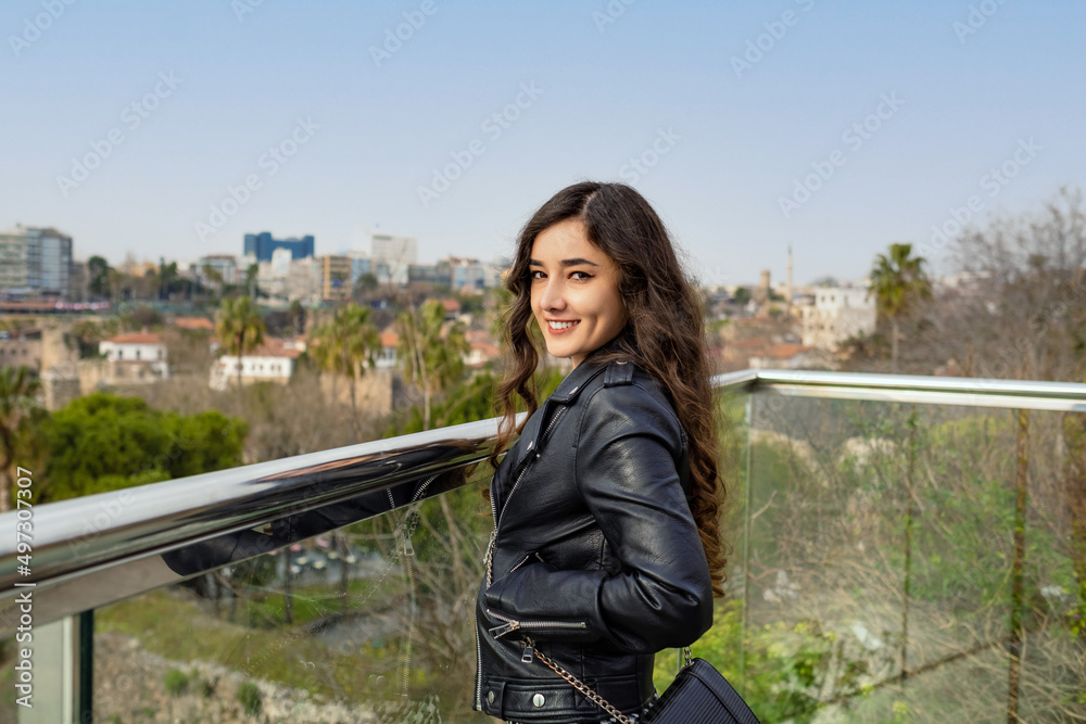 Posing, young woman poses on a high balcony against the view, young adult smiling at camera enjoying vacation
