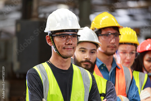 A team of male and female engineers wearing safety helmets. Standing in an industrial factory