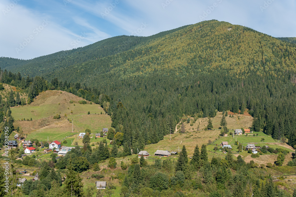 Aerial view on the hills, mountains, green forest and houses in a small village on a bright sunny day Aerial view on the hills, mountains, green forest and houses in a small village on a bright sunny day