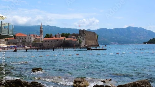 Resting people on sandy Brijeg od Budva beach on background of old city walls fortress. Old Town of Budva is situated on a rocky peninsula. Summer sunny landscape. Montenegro photo