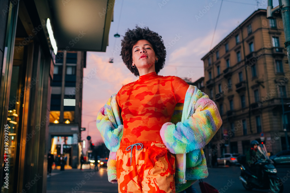Proud young black woman posing outdoor city night strong and confident hands on hips