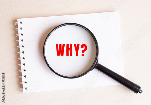 The magnifying glass lies on the notebook and shows the inscription WHY on a white page.