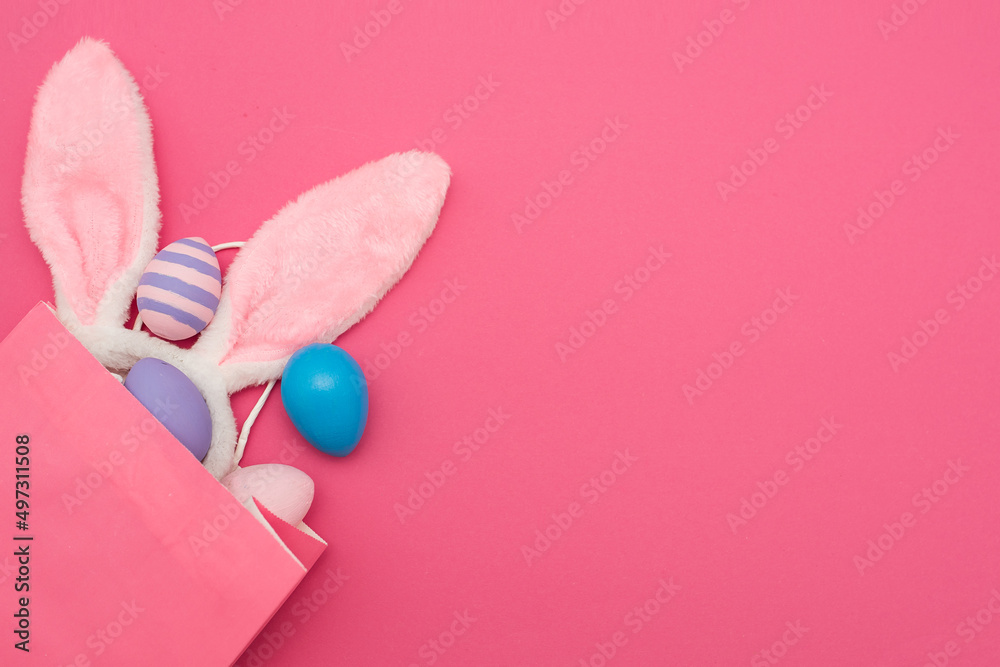 The concept of an online store for Easter, purchases and sales for the Easter holiday. Pink gift bag with bunny ears and colored eggs on a pink background, a place for text.