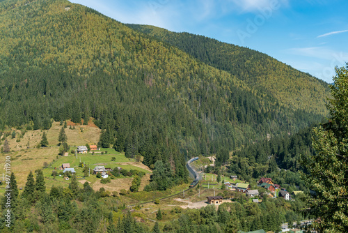 Aerial view of the railway station in the mountains with a train passing by green forest and houses in a small village on a bright sunny day