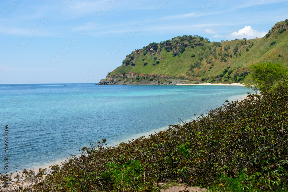 The stunning turquoise ocean and crystal clear water of Cristo Rei Back Beach surrounded by green hills during wet season in capital Dili, Timor Leste
