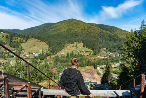 A guy is sitting at the top of a ski downhill in the mountains and enjoying breathtaking view
