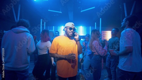 An African-American man talking on the phone in a nightclub on the dance floor under the light of colored spotlights. Night club