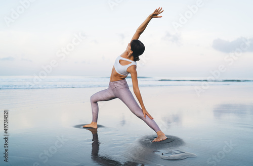 Motivated female in sportive tracksuit exercising during pilates slimming at coastline beach, Caucasian fit girl reaching healthy lifestyle and wellbeing vitality while stretching during yoga