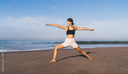 Flexible female in sportswear have yoga training at seashore beach spending daytime for reaching vitality wellness, beautiful Caucasian woman recreating during morning stretching at seashore beach