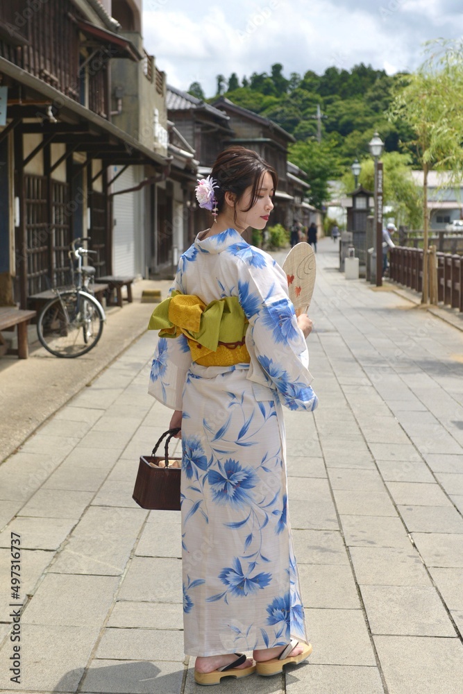 うちわを手に小江戸佐原の町並みでポーズをとる浴衣を着た振り向く若い女性の後ろ姿	