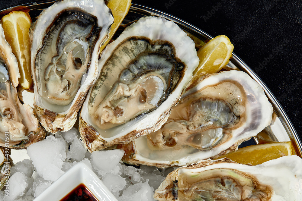 Oysters with lemon served on black round platter. Luxury delicatessen seafood. Oysters with lemon served on black round platter. Luxury delicatessen seafood.