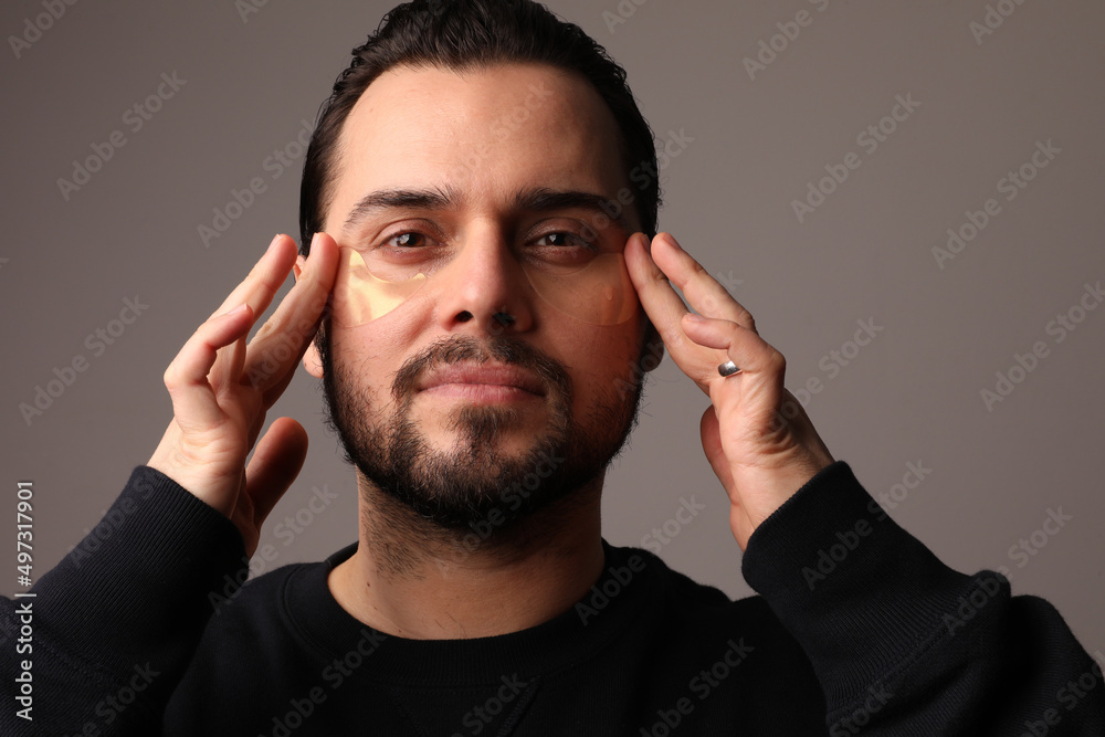 Portrait of attractive well-groomed guy wearing eye patches modern uplift rejuvenation effect isolated on light white background. 