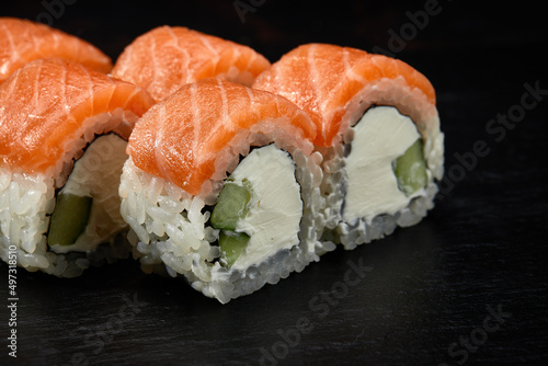 Philadelphia roll sushi with salmon, cucumber and cream cheese on black background for menu. Japanese food
