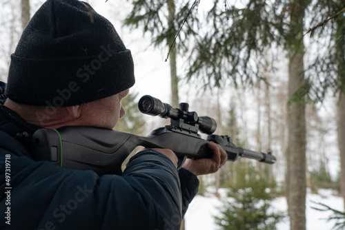 A man with a rifle in the spring forest, the hunter holds a rifle and waits for prey, the hunter shoots photo