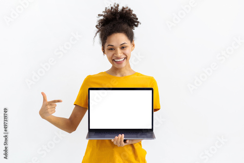 Portrait of young African American woman with laptop on white background. Beautiful female points her finger at a blank laptop screen, looking at the camera and smiling