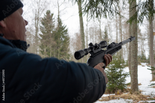 A man with a rifle in the spring forest, the hunter holds a rifle and waits for prey, the hunter shoots