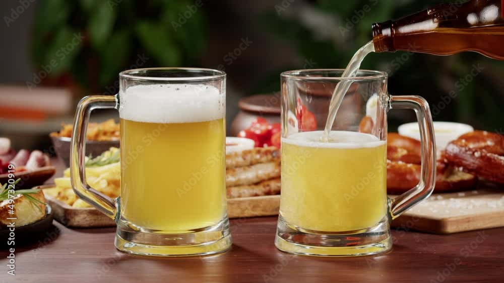 Pouring beer in glasses close-up. Traditional German Cuisine. Smoked sausages with fried potatoes, pickled cucumbers, bratwursts and fresh pretzels on table. Cooked National Czech Food. Pouring beer in glasses close-up. Traditional German Cuisine. Smoked sausages with fried potatoes, pickled cucumbers, bratwursts and fresh pretzels on table. Cooked National Czech Food.