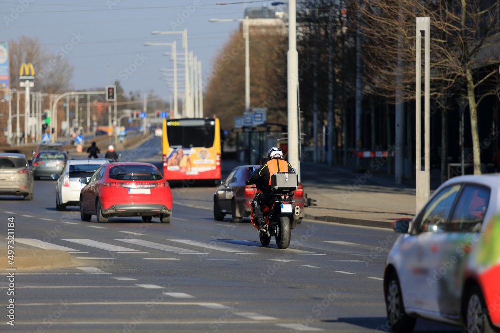 Motocyklista z bagarznikiem jedzie ulicą Wrocławia. - obrazy, fototapety, plakaty 