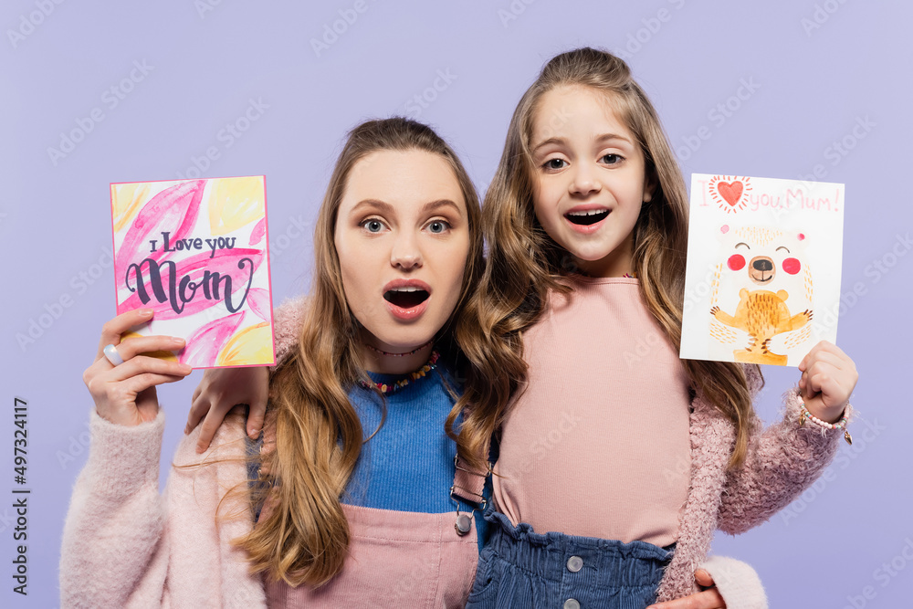 amazed mother and daughter holding greeting cards isolated on purple, mothers day concept. amazed mother and daughter holding greeting cards isolated on purple, mothers day concept.