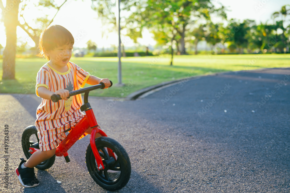 Baby boy riding balance bike in park with soft-focus and over light in the background Baby boy riding balance bike in park with soft-focus and over light in the background