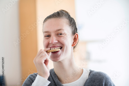 Junge Frau mit blonden Haaren  Dutt  isst einen Keks in  der Wohnung