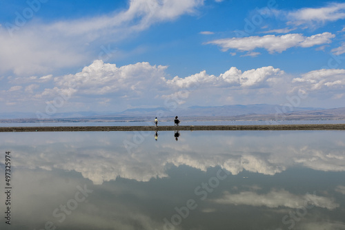 mother and son sitting on small island in front of van lake in turkey, clouds and blue sky reflect in water