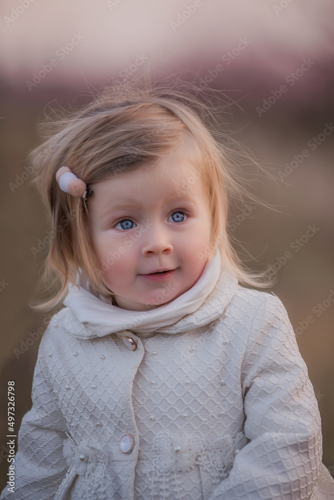Little toddler girl in white coat stands in field, among blooming peach rose gardens at sunset Little toddler girl in white coat stands in field, among blooming peach rose gardens at sunset
