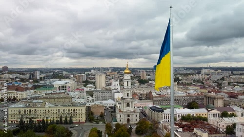 Flag of Ukraine waving on flagpole with autumnal epic gray cloudscape. Left to right city aerial view on river Lopan embankment, Dormition Cathedral in Kharkiv, Ukraine photo