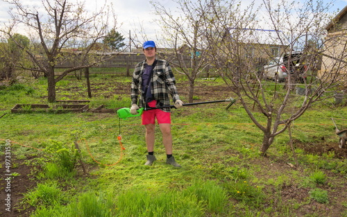 junger gutaussehender Mann mäht das Gras mit einem elektrischen Trimmer auf seinem Grundstück Frühlingstag photo