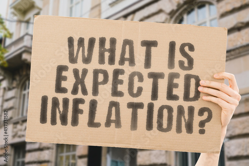 The question " What is expected inflation? " on a banner in men's hands with blurred background.  Data. Economic. Future. Grow. Plan. Price. Profit. Rate. Stock. Wish. Cost. Achieve. Analysis. Crisis © AndriiKoval