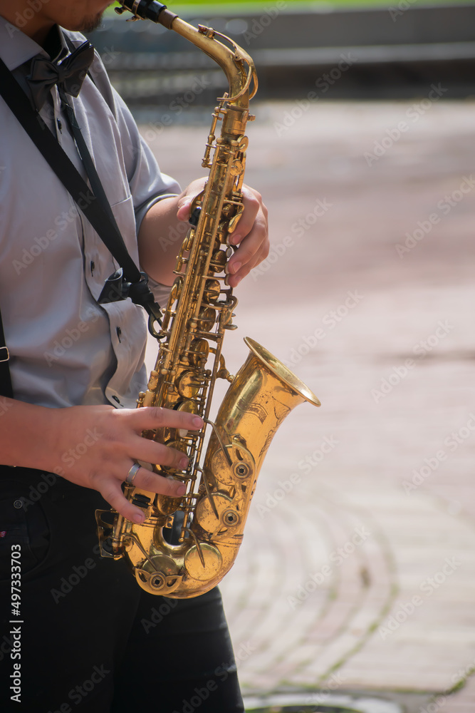 Fototapeta premium Man in blues or jazz suit, with black tie and black trousers playing a saxophone in public with asphalt background.