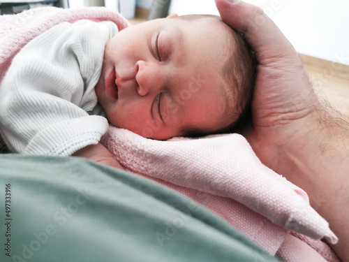 Fathers hand holding his daughters head in hospital after birth.