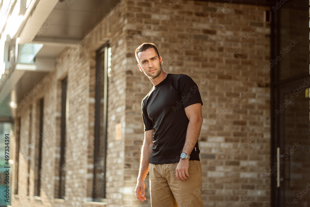 handsome man with short bristles in a black T-shirt on a brick wall