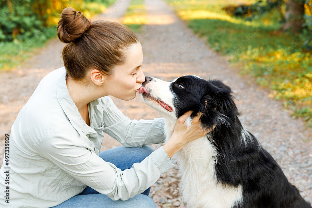 Smiling young attractive woman playing with cute puppy dog border collie on summer outdoor background. Girl holding embracing hugging dog friend. Pet care and animals concept Smiling young attractive woman playing with cute puppy dog border collie on summer outdoor background. Girl holding embracing hugging dog friend. Pet care and animals concept