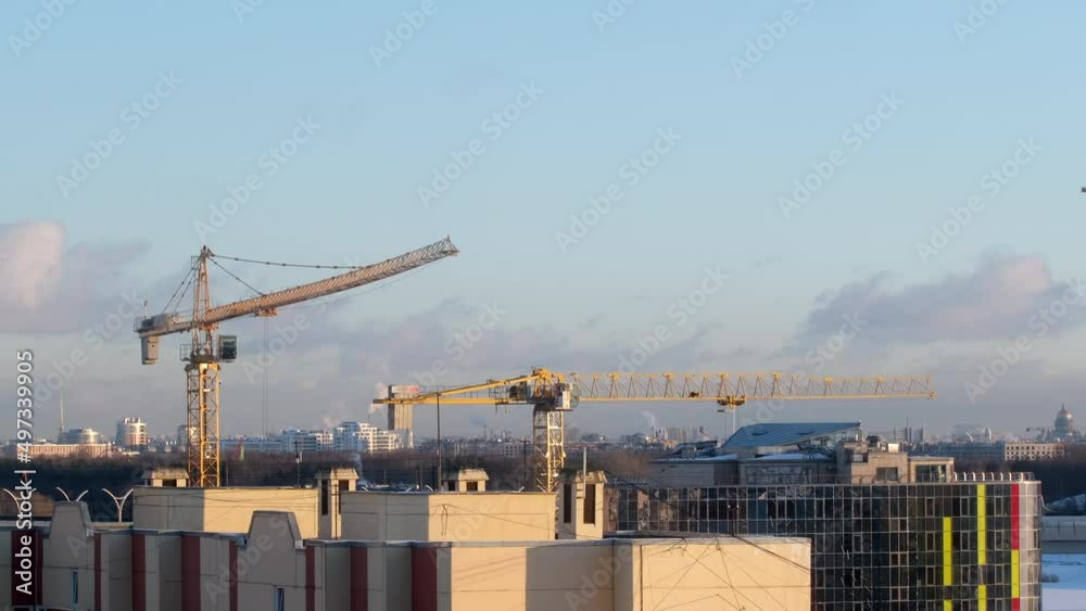 Cranes at a construction site lift loads against the background of a city and a beautiful sky with a dawn with clouds. Construction of industrial and residential facilities Cranes at a construction site lift loads against the background of a city and a beautiful sky with a dawn with clouds. Construction of industrial and residential facilities