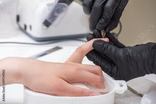 Manicurist removing cuticle from female nails by metal pusher during soaking fingernails in the bath at nail salon. Hands during a manicure care session in a spa salon. Nail care