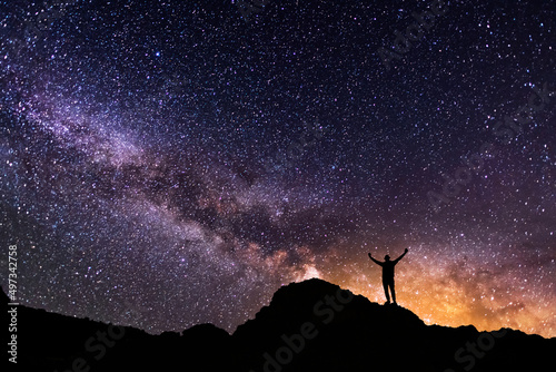 Silhouette of a hiker on the hill in starry night sky. Bright milky way galaxy behind him.