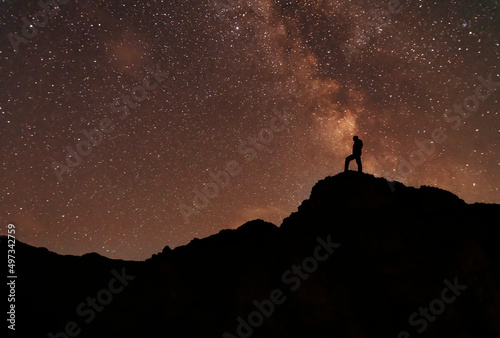 Silhouette of a hiker on the hill in starry night sky.  Bright milky way galaxy behind him.