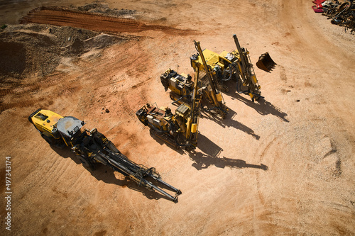 Yellow drilling rigs using to drill holes during blasthole drilling operations parked on dirt parking lot aerial view