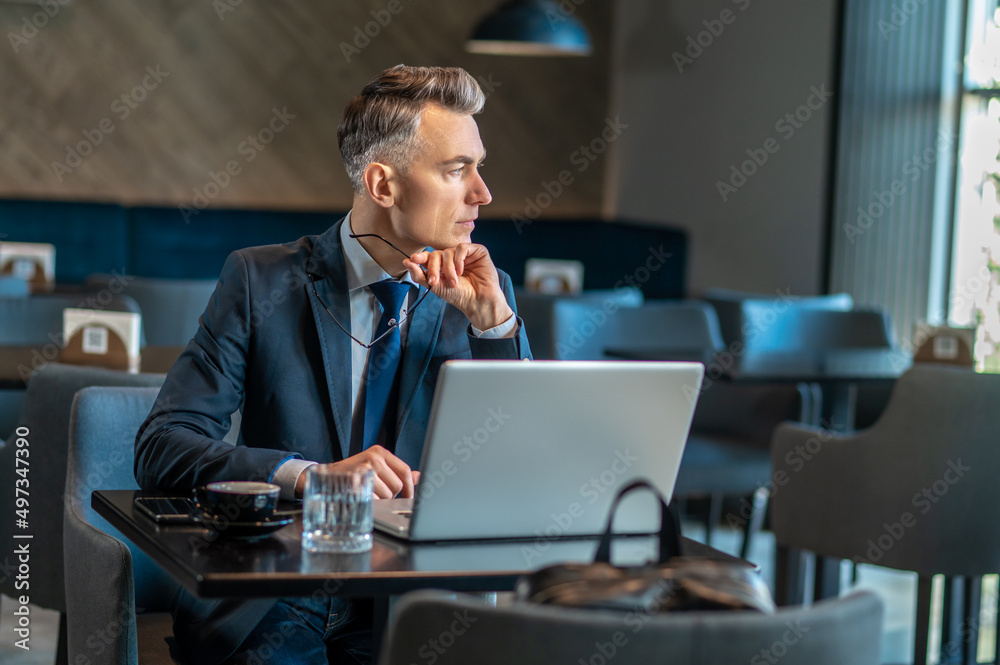 A mid aged businessman sitting at the laptop and thinking