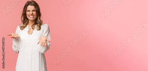 Portrait of dissatisfied, disappointed cute girl in white dress, cringe show tongue, smell something awful, pointing with raised hands at bad unappropriate thing, grimacing dislike, pink background photo