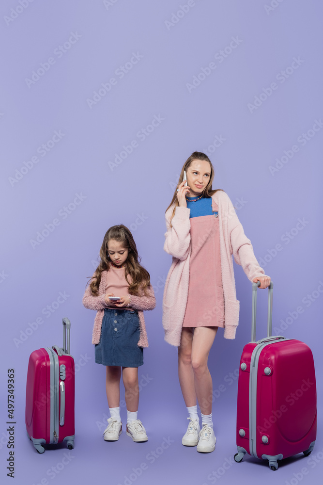 full length of mother and child using smartphones near baggage on purple. full length of mother and child using smartphones near baggage on purple.