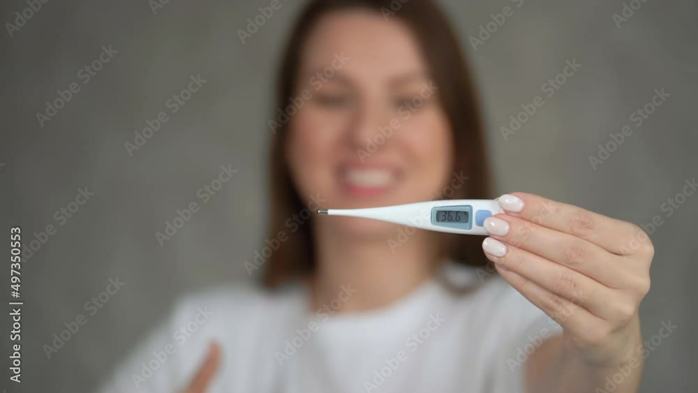 Woman holds an electronic thermometer in her hands, showing 36.6 degrees Celsius Woman holds an electronic thermometer in her hands, showing 36.6 degrees Celsius
