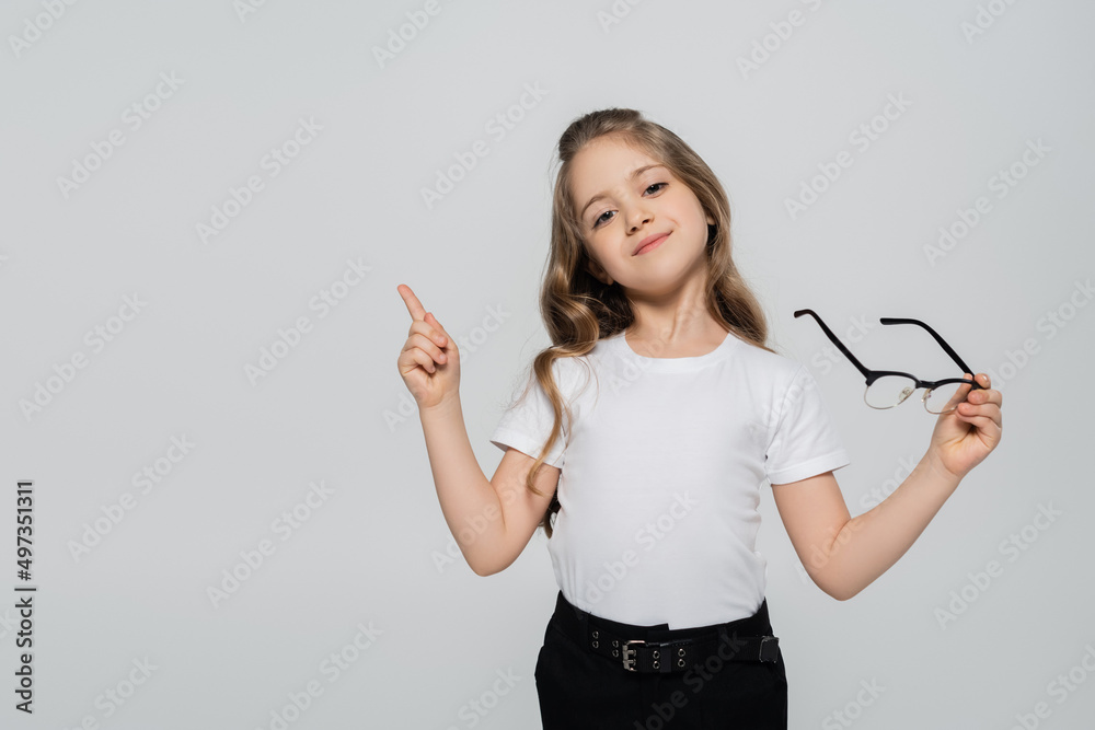 smiling child holding eyeglasses and pointing with finger isolated on grey. smiling child holding eyeglasses and pointing with finger isolated on grey.