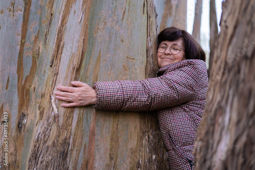 A senior woman framed between trunks and hugging a tree