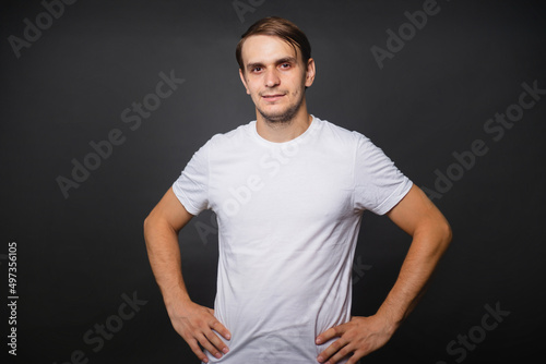 A handsome young man in a white t-shirt stands on a gray background. mockup