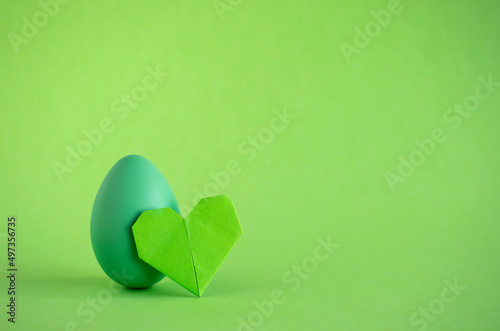 Easter egg and origami heart on green backgorund. Copy space.