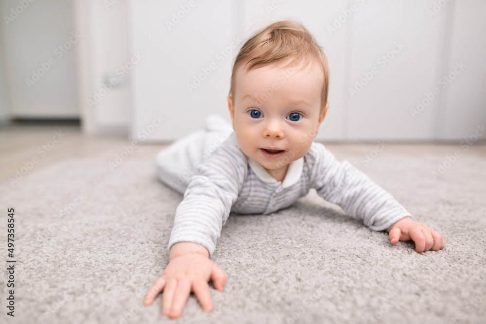 Charming newborn baby in a bodysuit lies on his stomach on a soft carpet. Happy baby lying on his stomach, textiles and bedding for children Charming newborn baby in a bodysuit lies on his stomach on a soft carpet. Happy baby lying on his stomach, textiles and bedding for children