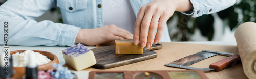 Cropped view of craftswoman making soap on cutting board near supplies, banner.
